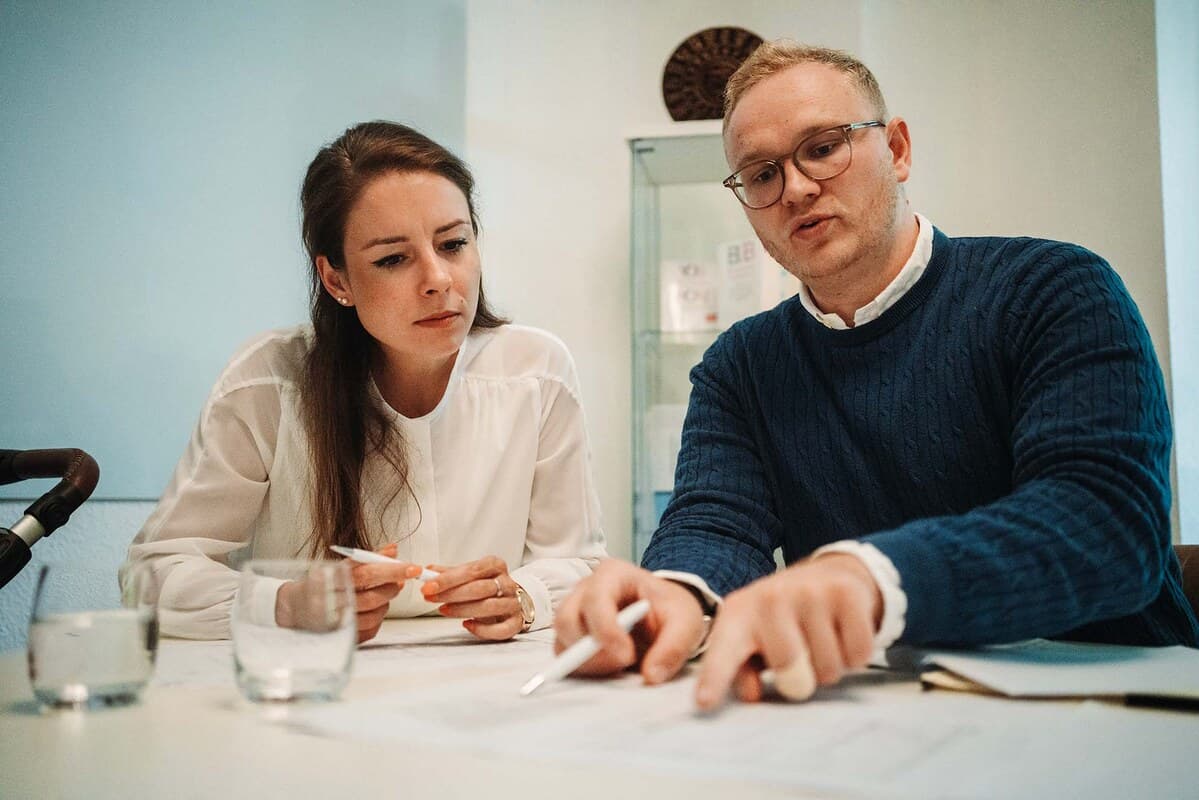 Auswertung der Objektunterlagen am Besprechungstisch: Grundriss und Dokumente werden für die Erstellung eines Immobiliengutachtens gemeinsam durchgegangen.